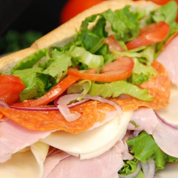 Close-up of a large Italian sub sandwich with ham, salami, cheese, lettuce, tomatoes, and onions.