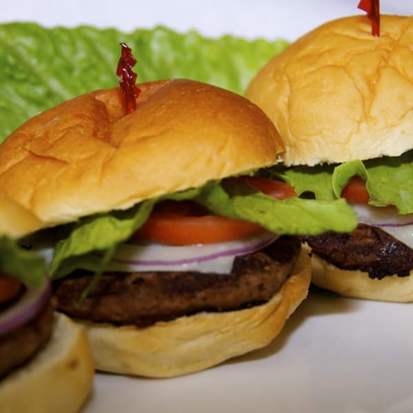 Three mini burgers with lettuce, tomato, and onion, on a white plate with green lettuce.