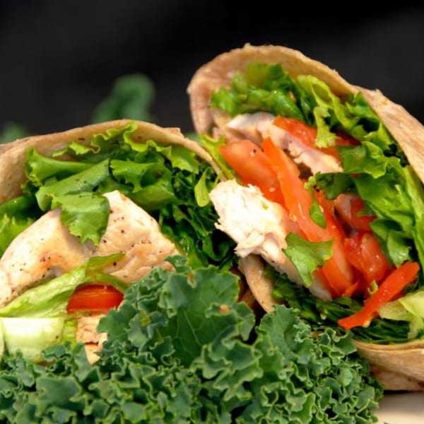 Two chicken wraps filled with fresh lettuce, tomatoes, and chicken pieces, garnished with kale.