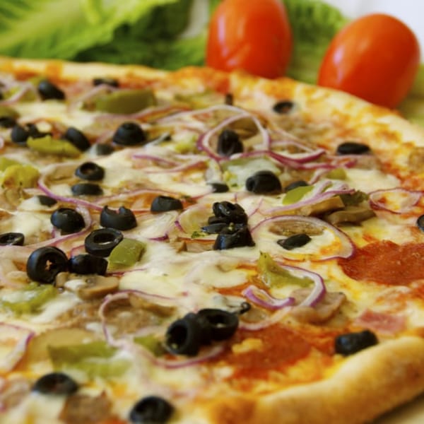 A close-up of a New York-style pizza with pepperoni, olives, onions, and peppers.